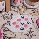 Teapot-shaped tic-tac-toe game with floral designs on a lace tablecloth