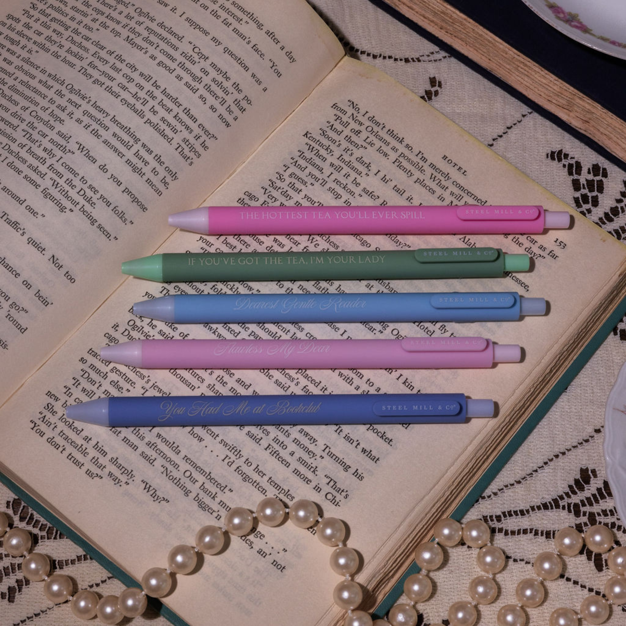 Set of colorful pens on an open book with a pearl necklace.