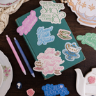 Teal notebook with decorative stickers on a wooden surface with tea-themed items.