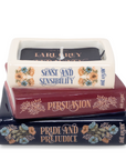 Stack of books with candles labeled 'Pride and Prejudice', 'Persuasion', and 'Sense and Sensibility' on a white background.