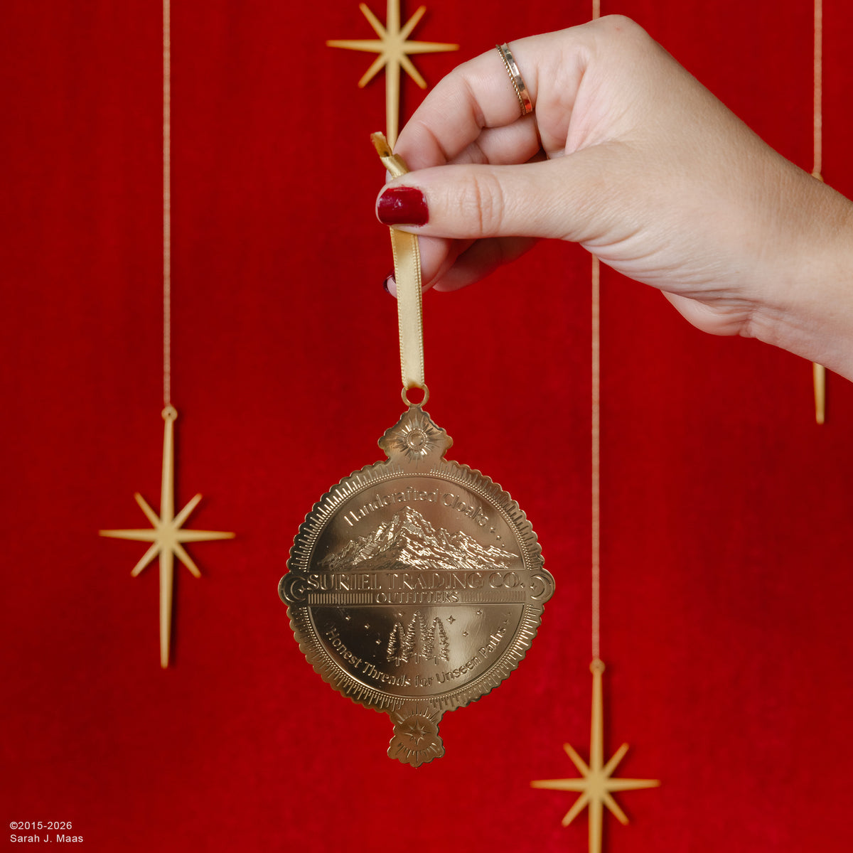 model holding suriel trading co. embossed gold ornament with gold hanging ribbon