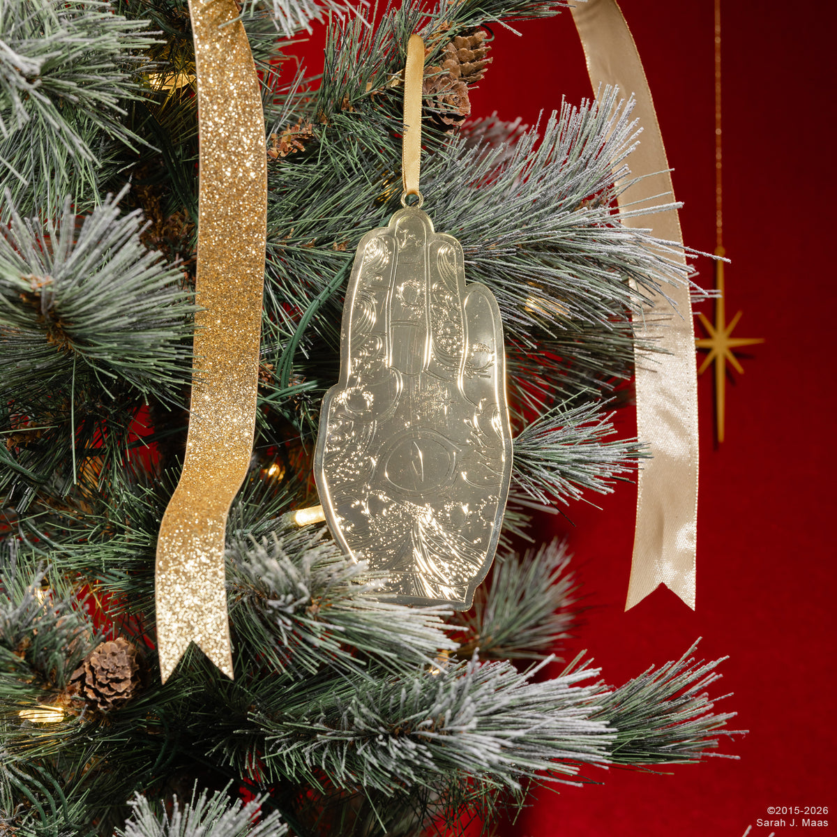 A gold-colored embossed  hand ornament  complete with a gold hanging ribbon hanging from a holiday tree