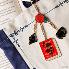 bag charm with enamel metal charms of a bow, cauldron, red rose, and ACOTAR book cover on a cream and navy tote bag