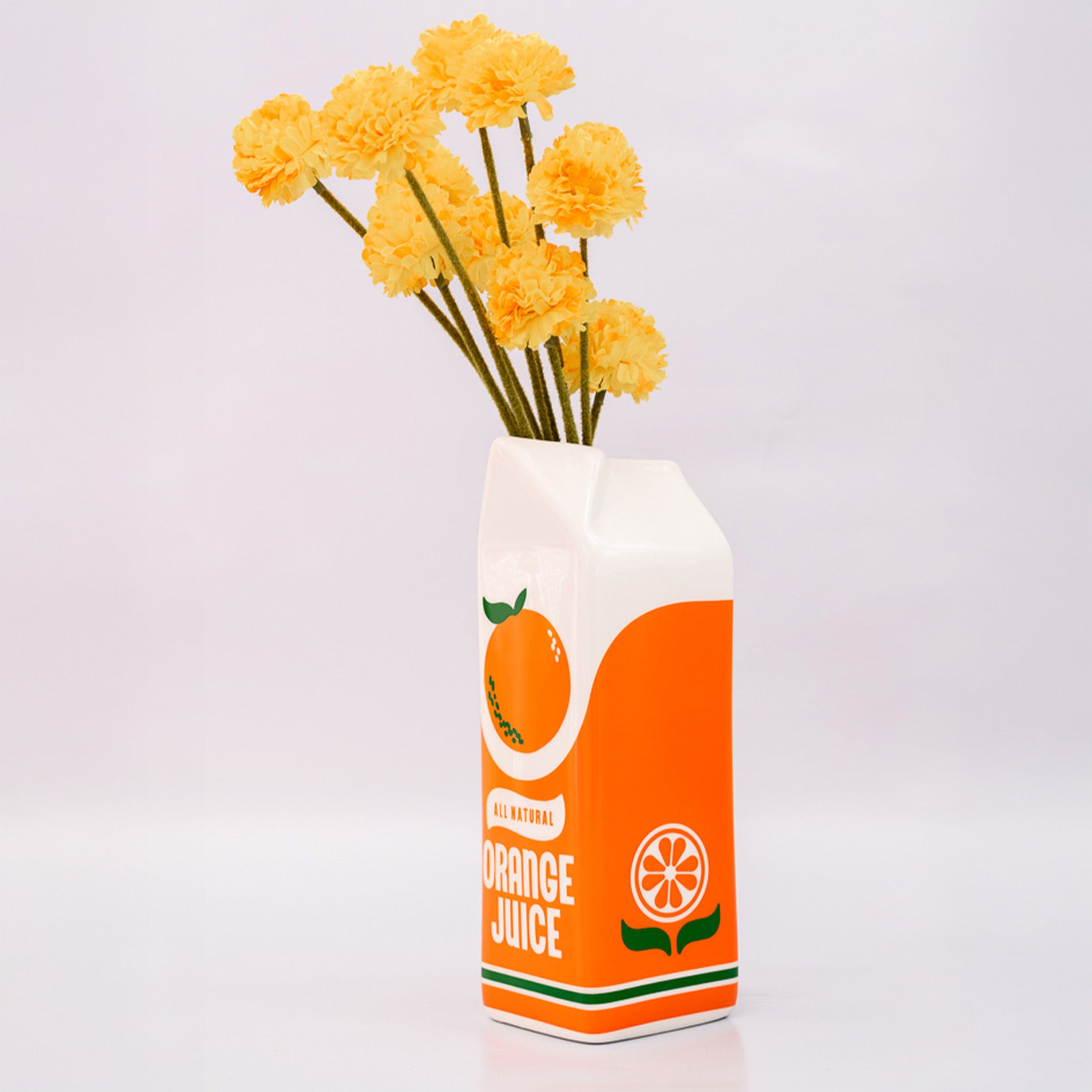 Orange juice carton vase with yellow flowers on a light gray background