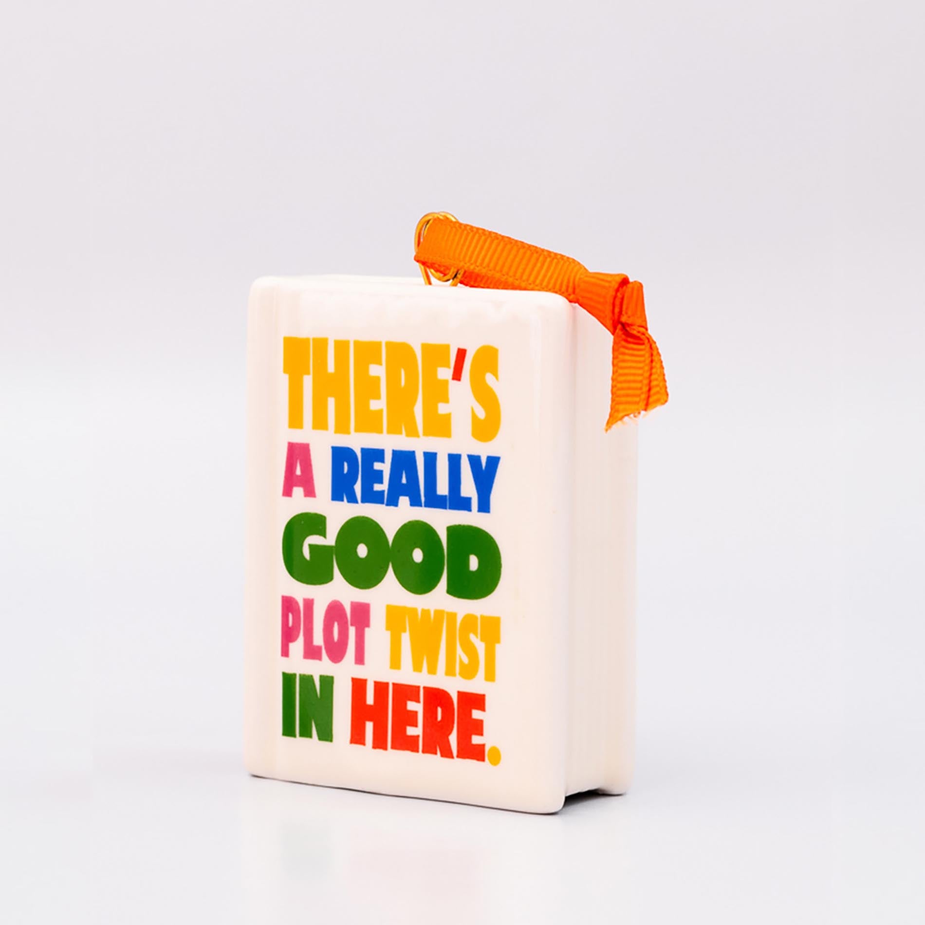 Sideview of ornament with 'THERE'S A REALLY GOOD PLOT TWIST IN HERE' and an orange hanger on a white background