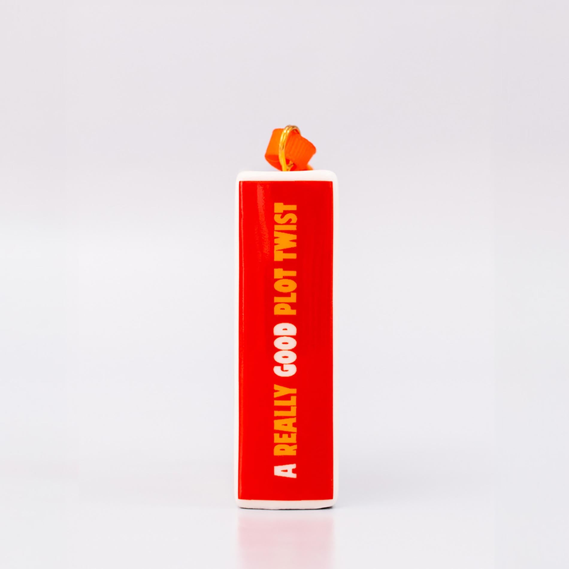 Spine of ornament with 'THERE'S A REALLY GOOD PLOT TWIST IN HERE' and an orange hanger on a white background