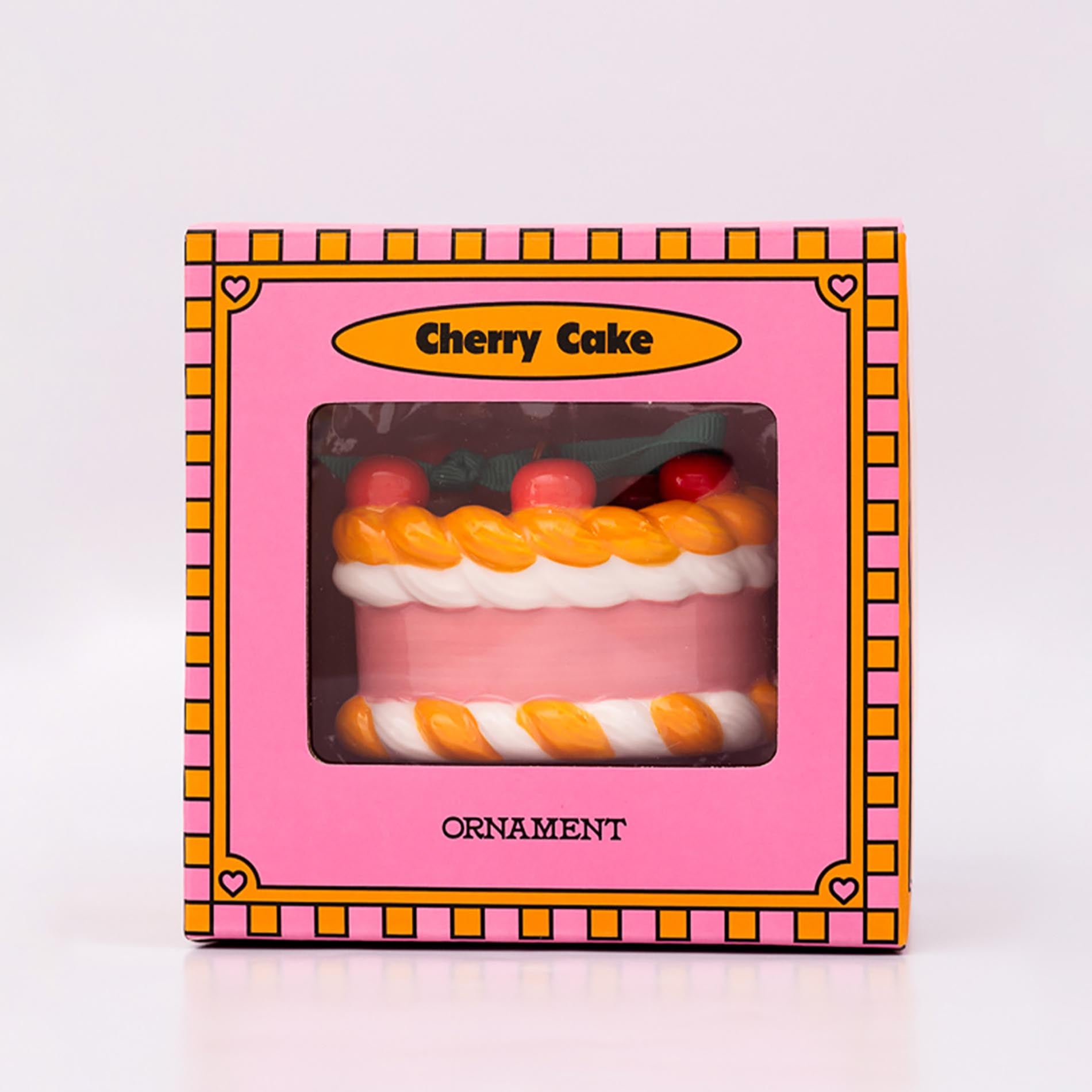 Packaged ornament cake with pink filling, orange and white striped sides, and red cherries on a white background
