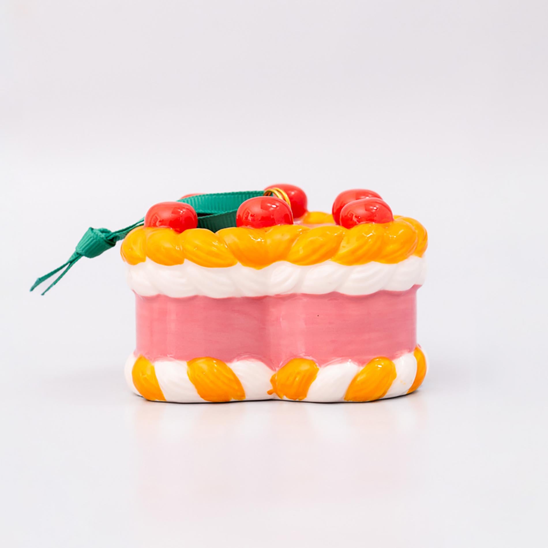 Sideview of ornament cake with pink filling, orange and white striped sides, and red cherries on a white background