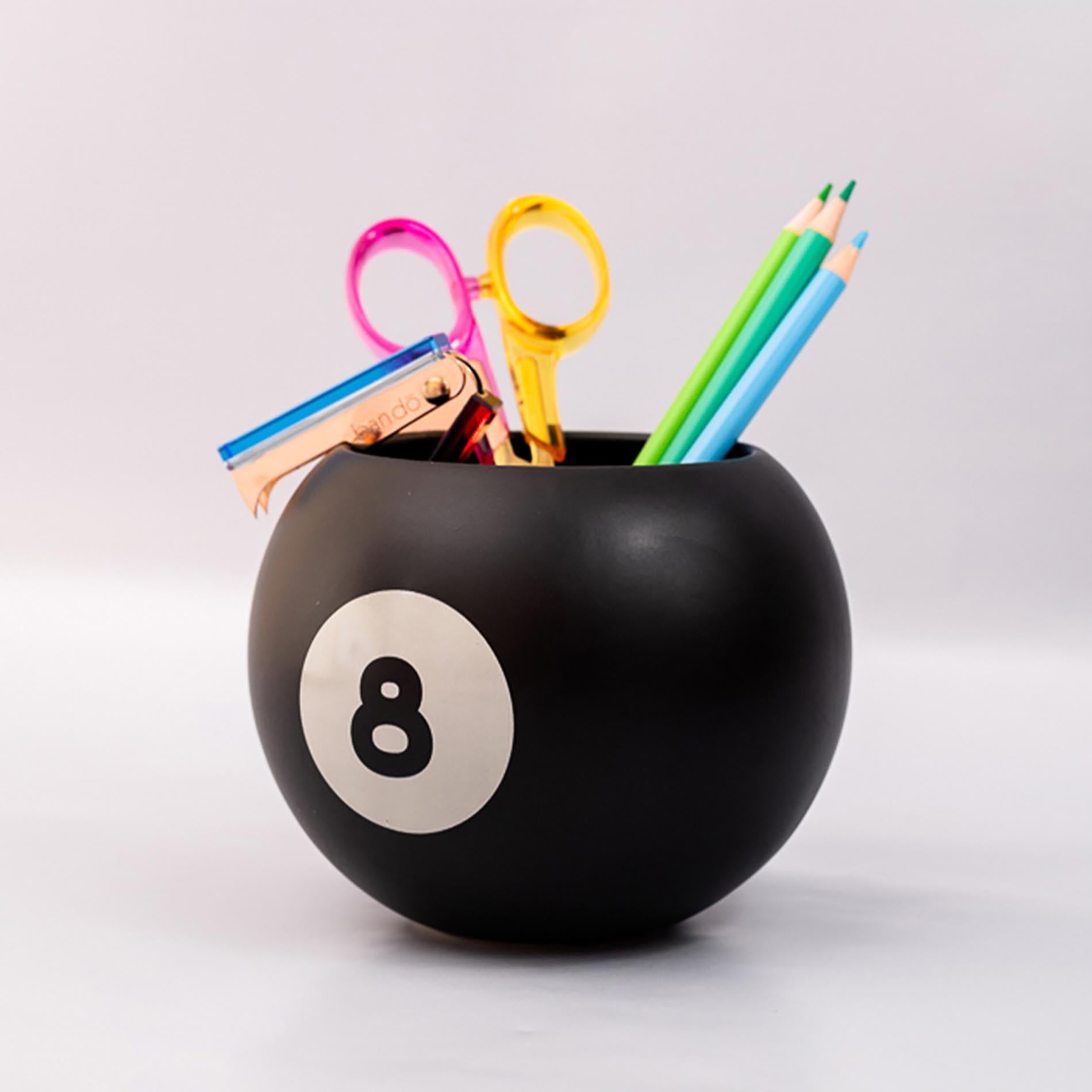 Black ball-shaped holder with number 8 holding colorful stationery items on a light gray background