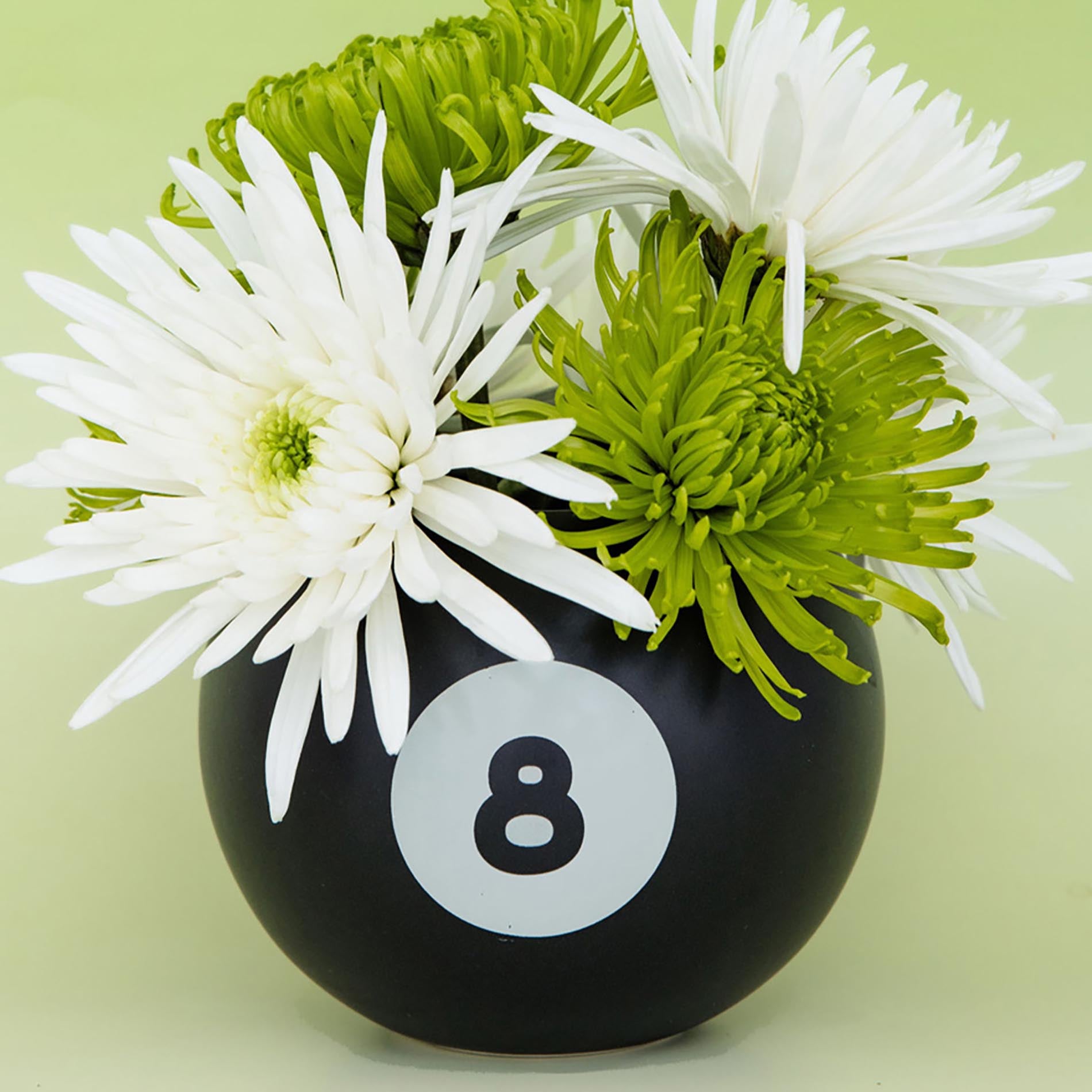 Black vase with number 8 and white and green flowers on a light green background