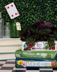 Stack of books with a plant on top, set against a green foliage background.