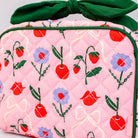 Pink quilted bag with cherry and flower pattern and green ribbon on a light gray background