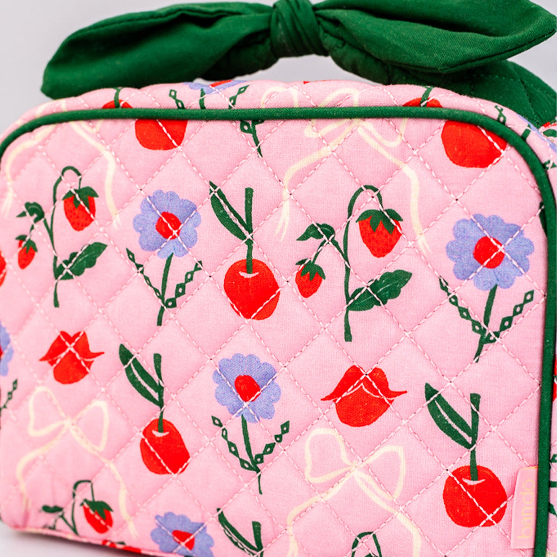 Pink quilted bag with cherry and flower pattern and green ribbon on a light gray background