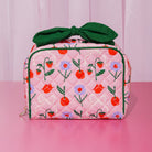 Pink quilted bag with floral and fruit patterns and a green bow on a pink background