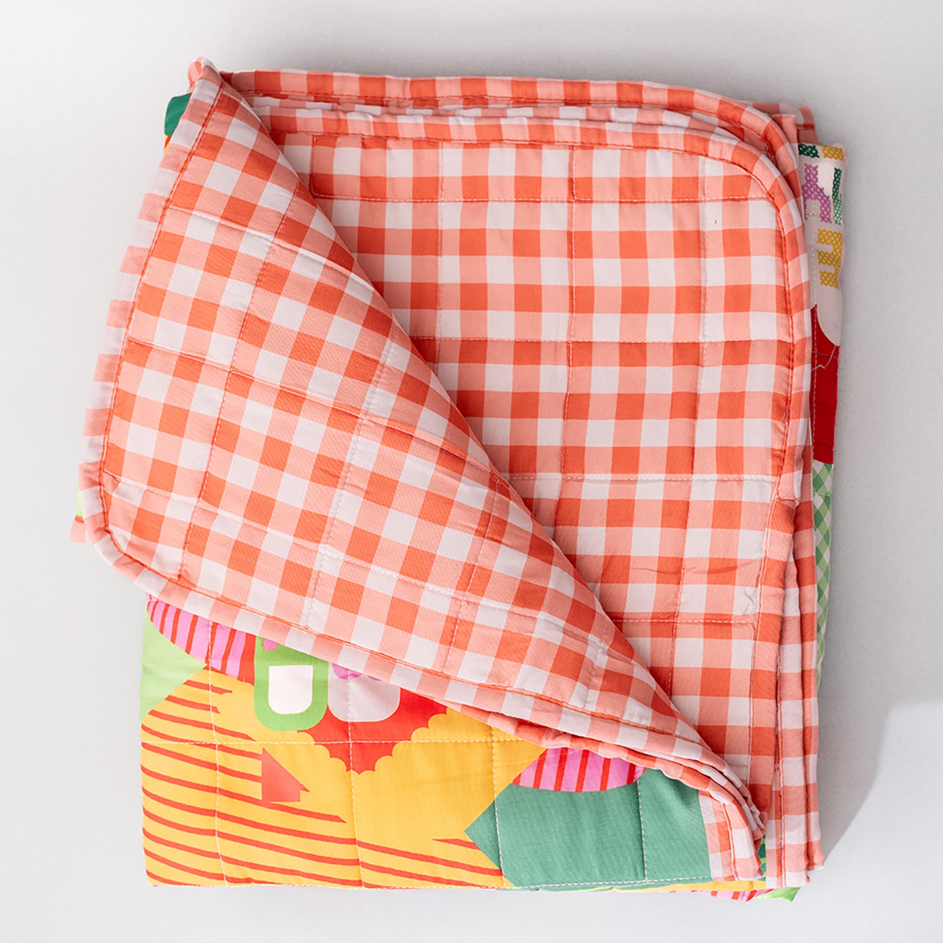 Folded quilt with orange and white checkered pattern on a light gray background
