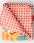 Folded quilt with orange and white checkered pattern on a light gray background