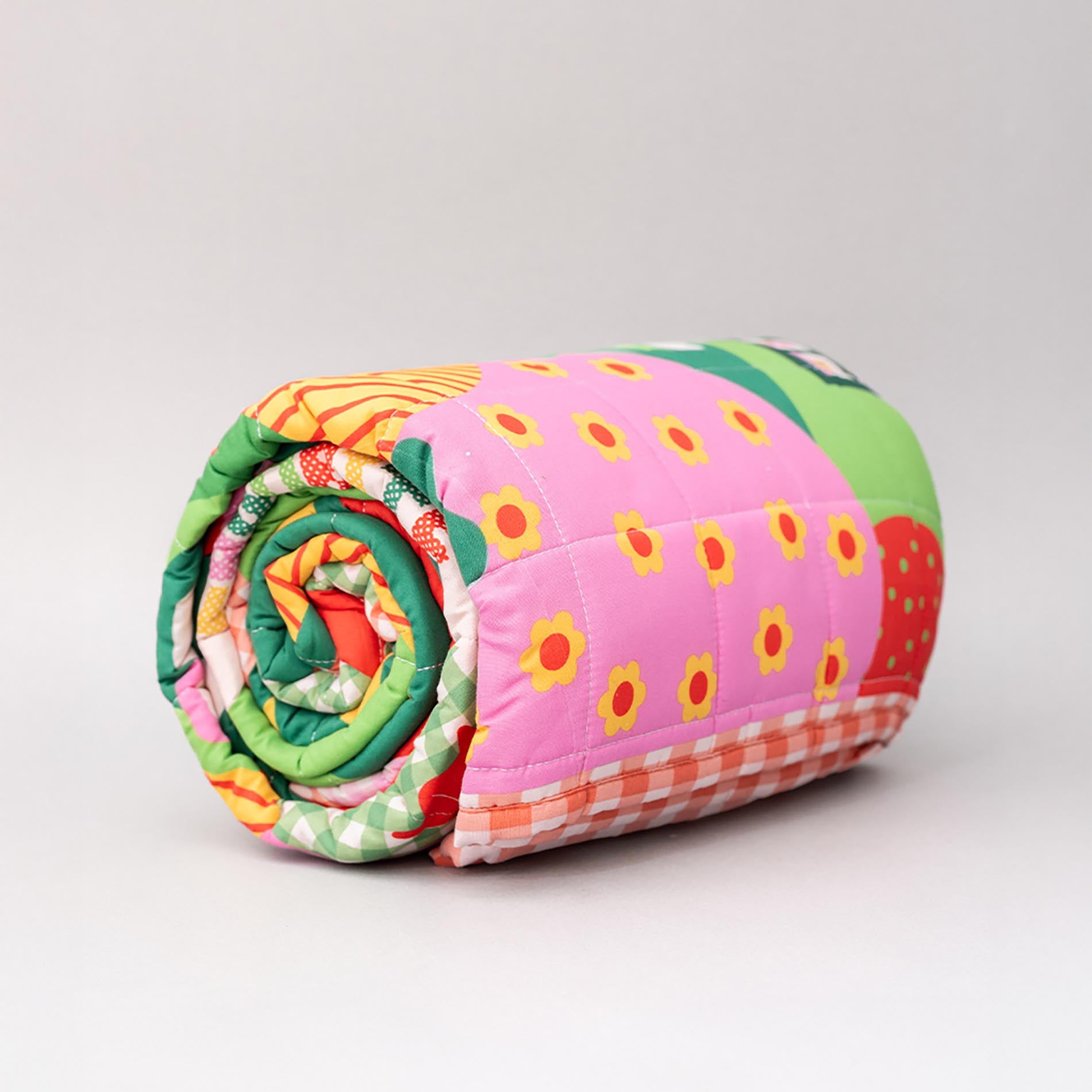 Rolled-up colorful quilt with strawberry pattern on a light gray background