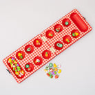 Red checkered mancala board with fruit-themed items on a light gray background