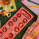 Red checkered mancala board with fruit-themed items on a grass