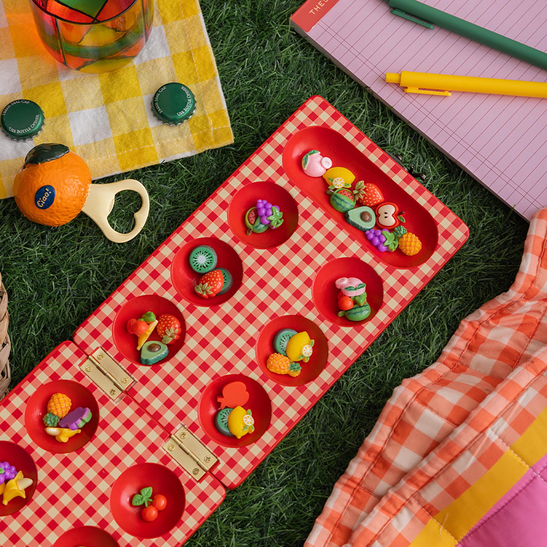 Red checkered mancala board with fruit-themed items on a grass