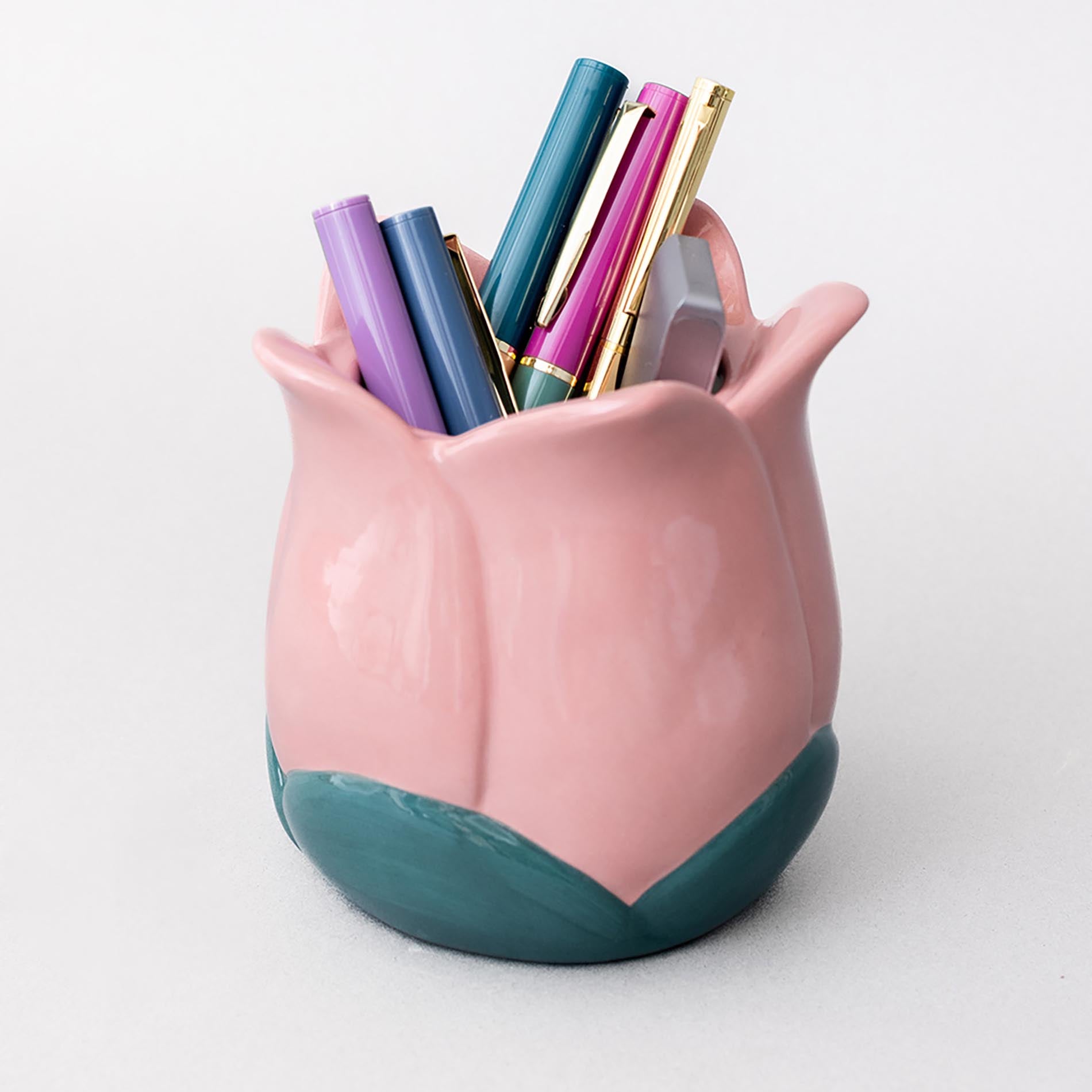 Pink tulip-shaped pen holder with colorful pens on a white background