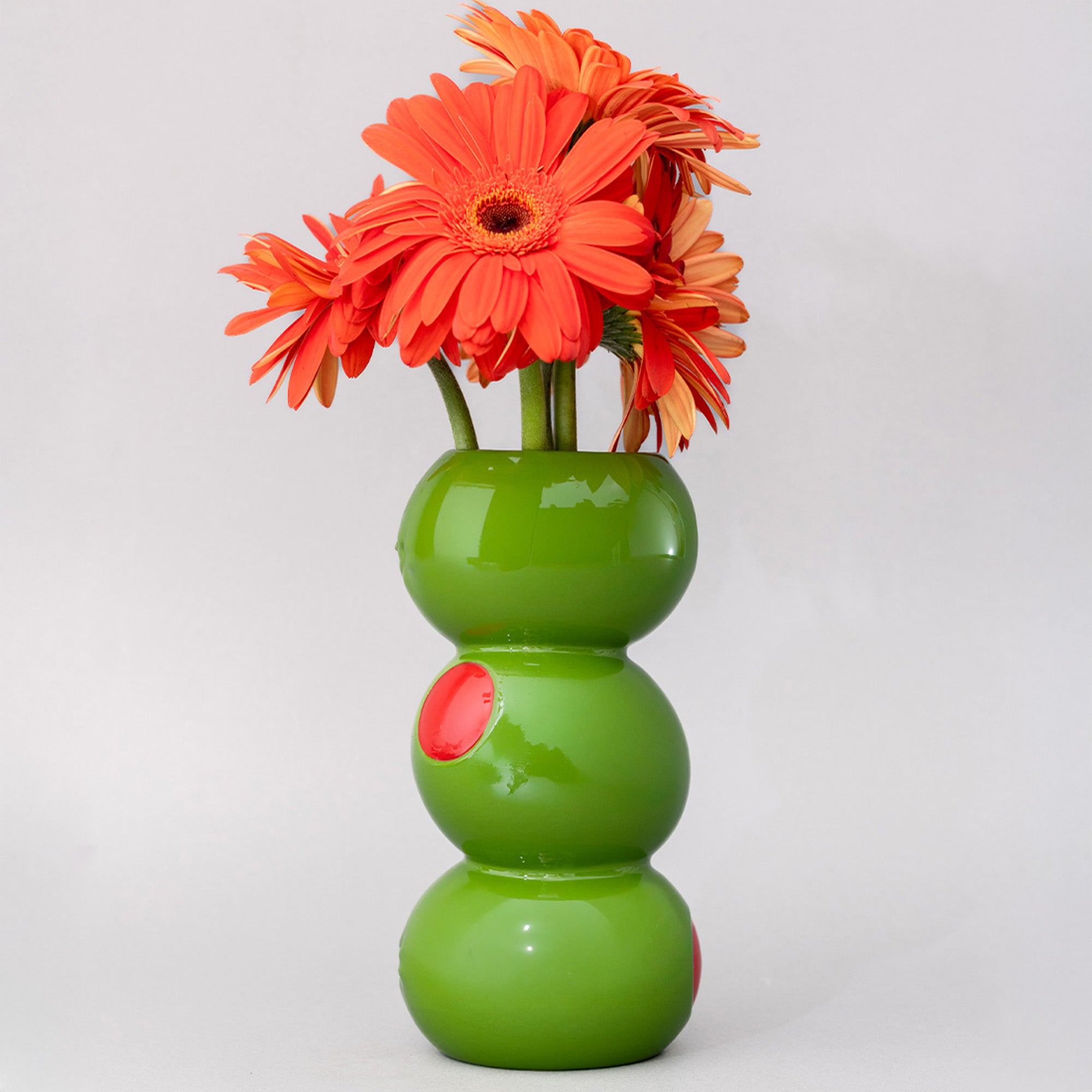 Green vase with three stacked sections holding orange flowers on a light gray background