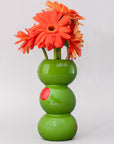 Green vase with three stacked sections holding orange flowers on a light gray background