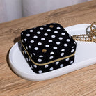 Black polka dot jewelry box with gold zipper on a white tray