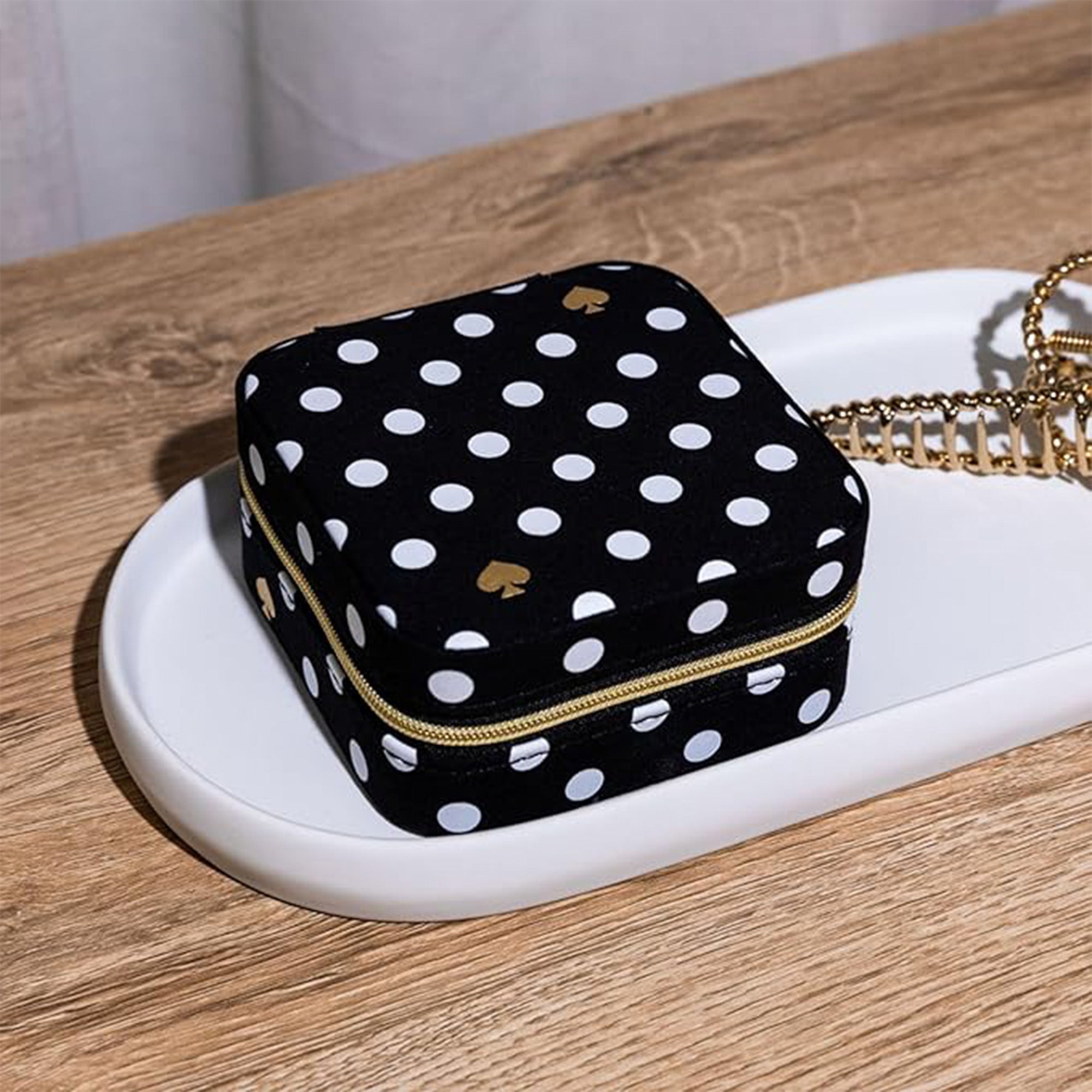 Black polka dot jewelry box with gold zipper on a white tray