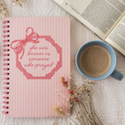 Pink notebook with decorative bow and text on a white background