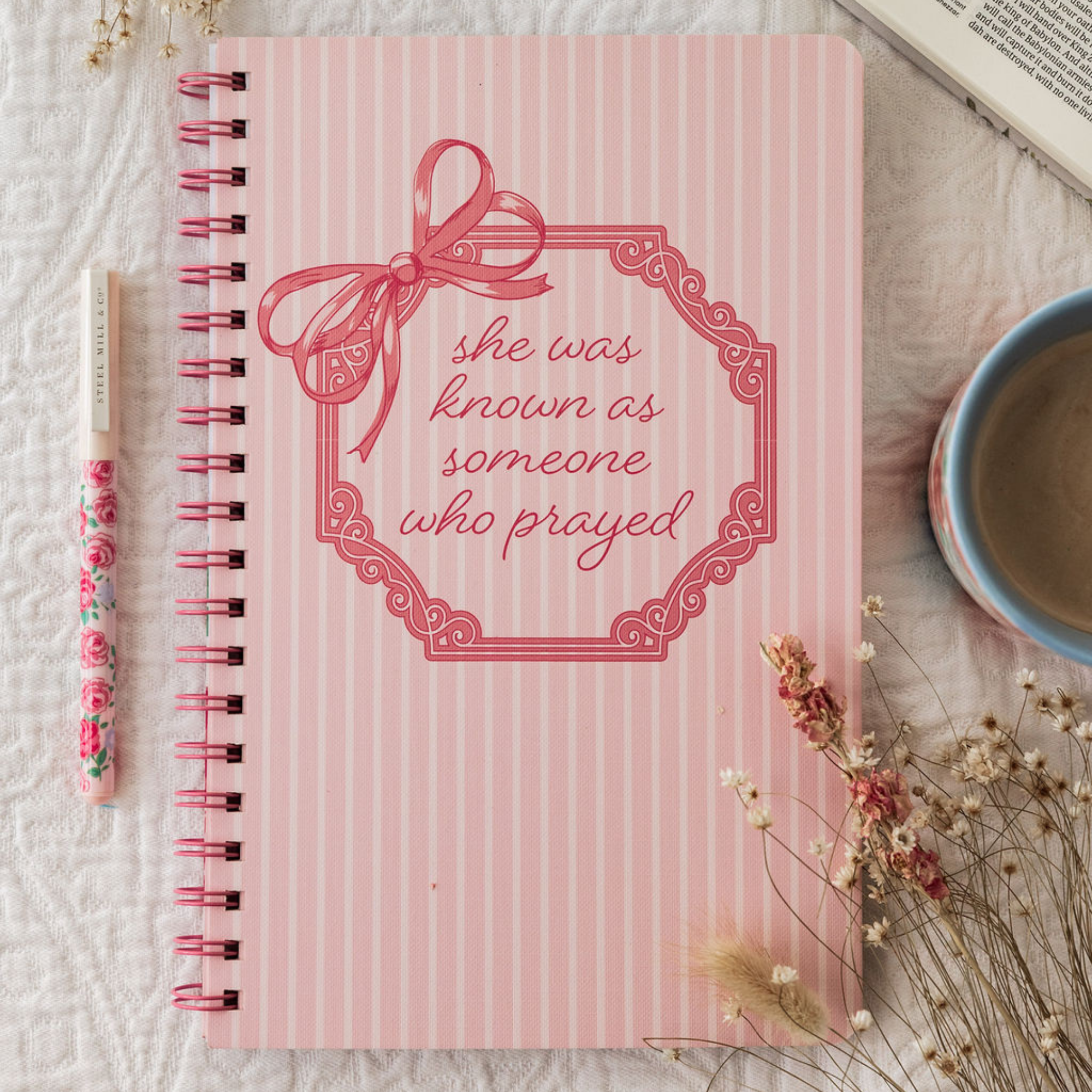 Pink notebook with decorative bow and text on a white background