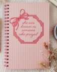 Pink notebook with decorative bow and text on a white background
