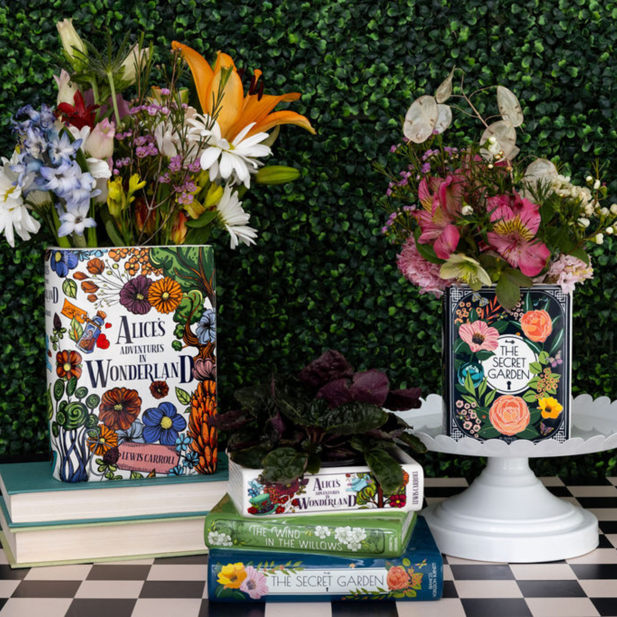 Books with floral designs on covers displayed against a green bush background.