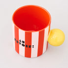 top view of red and white vertical stripe mug with yellow ball handle and double sided typography with 'BONJOUR!' on one side and 'AU REVOIR' on the other