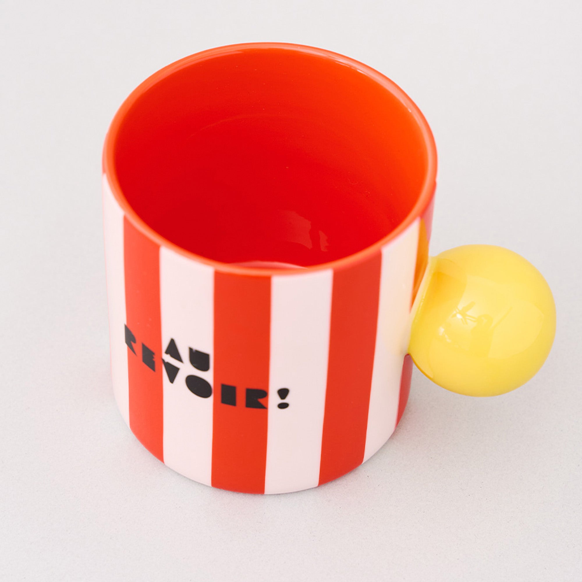 top view of red and white vertical stripe mug with yellow ball handle and double sided typography with 'BONJOUR!' on one side and 'AU REVOIR' on the other