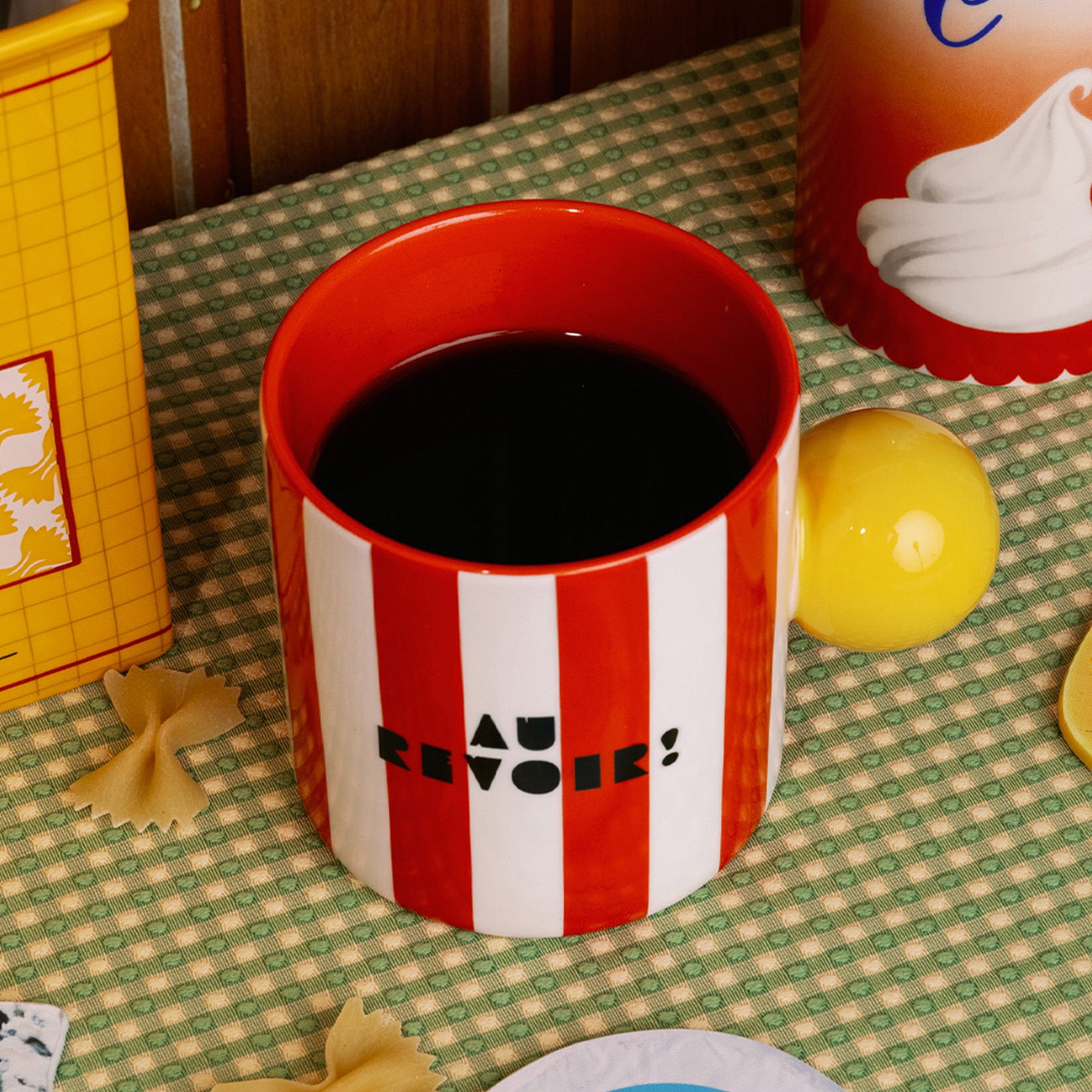 top view of red and white vertical stripe mug with yellow ball handle and double sided typography with 'BONJOUR!' on one side and 'AU REVOIR' on the other