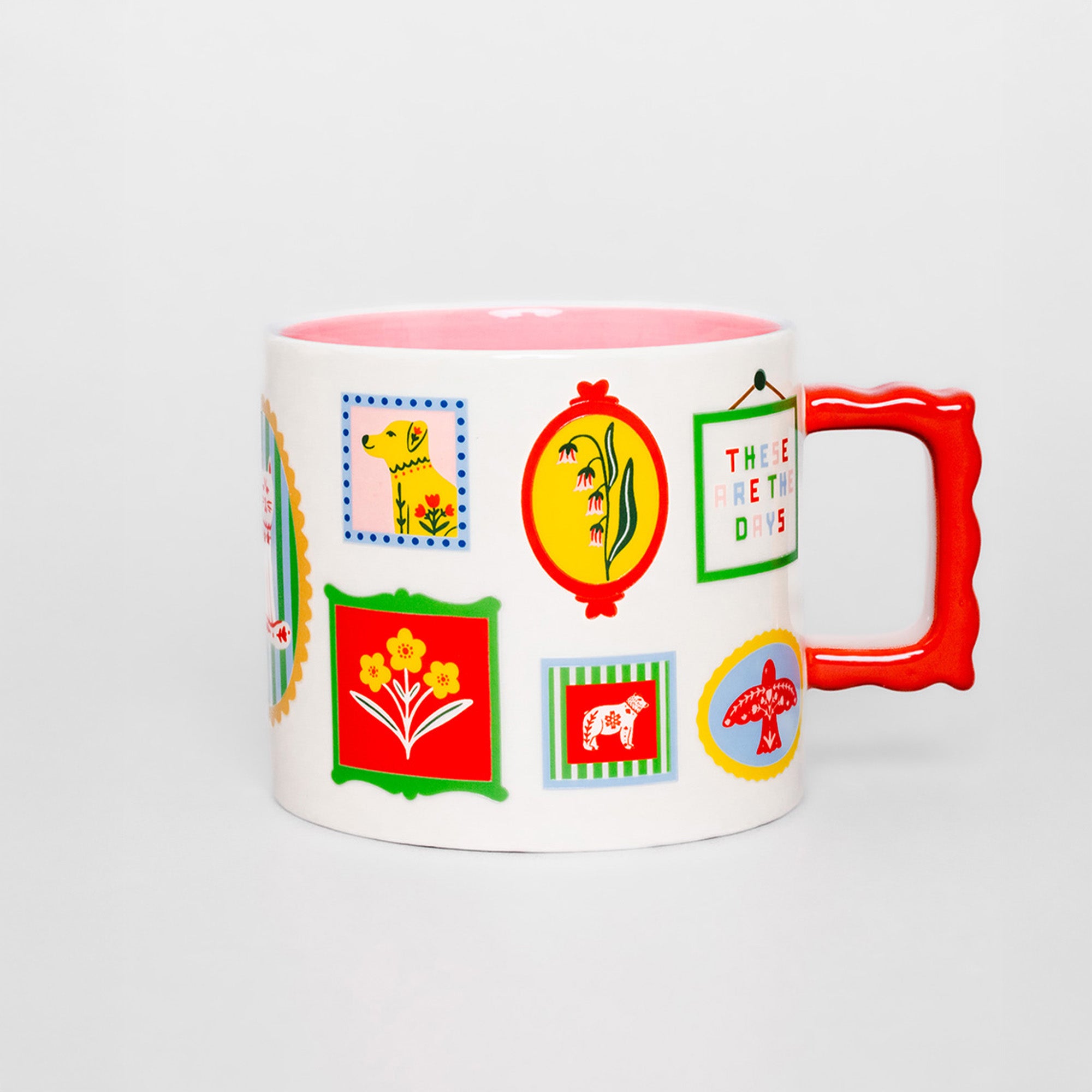 A white ceramic mug with a bright pink interior and a bold red handle, decorated with colorful retro-style illustrated patches and badges on the side.
