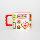 A white ceramic mug with a bright red handle and a pink interior, decorated with colorful tea-themed illustrations including teapots, cups, a butterfly, and framed prints, set against a light gray background.