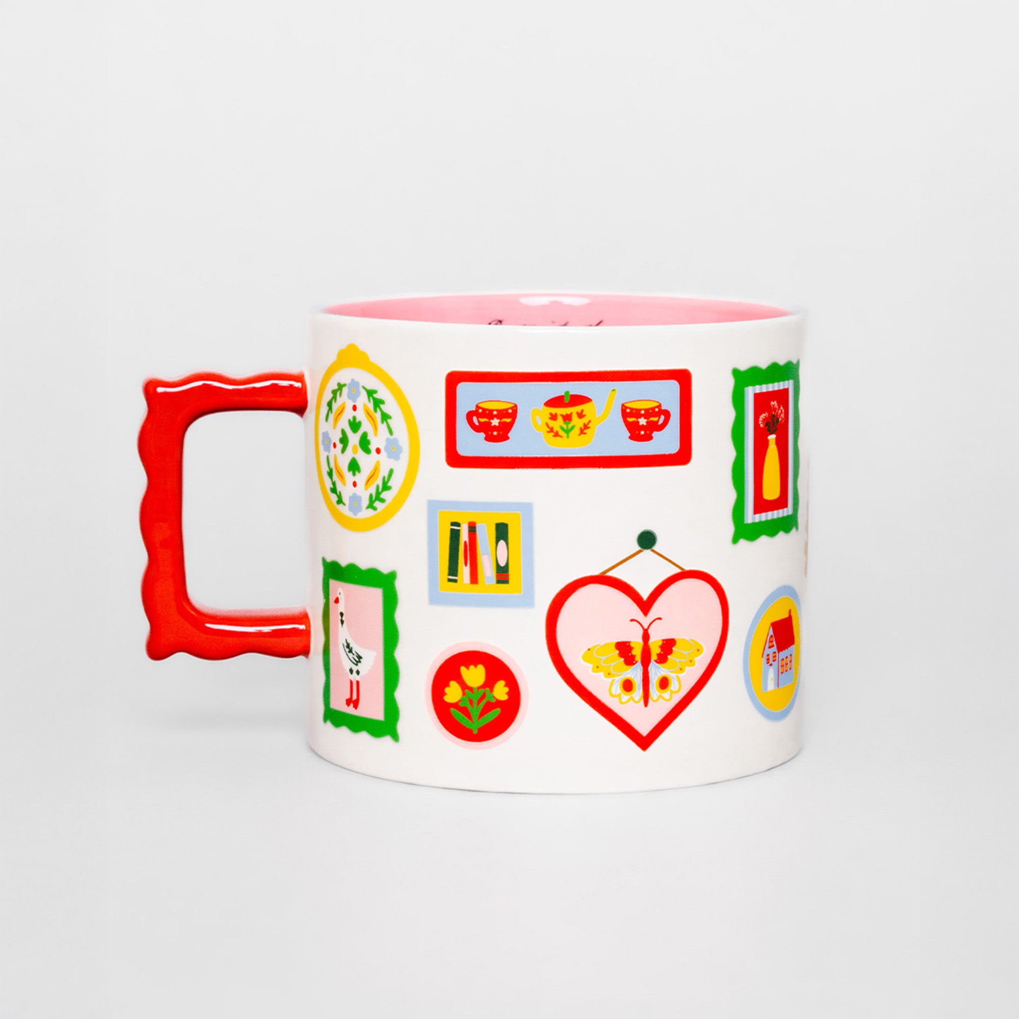 A white ceramic mug with a bright red handle and a pink interior, decorated with colorful tea-themed illustrations including teapots, cups, a butterfly, and framed prints, set against a light gray background.