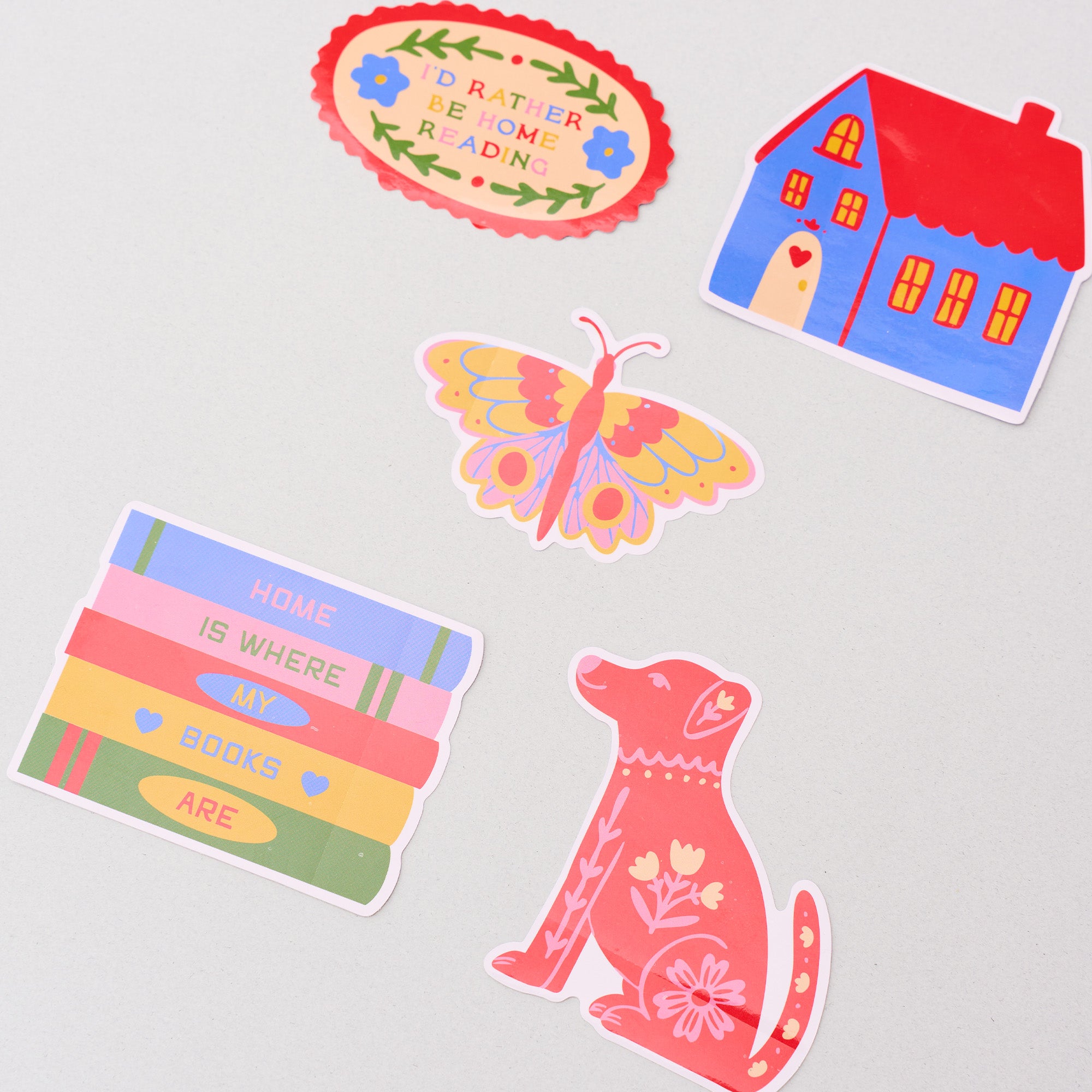 Set of colorful stickers including a butterfly, house, dog, and book-themed designs on a light gray background.