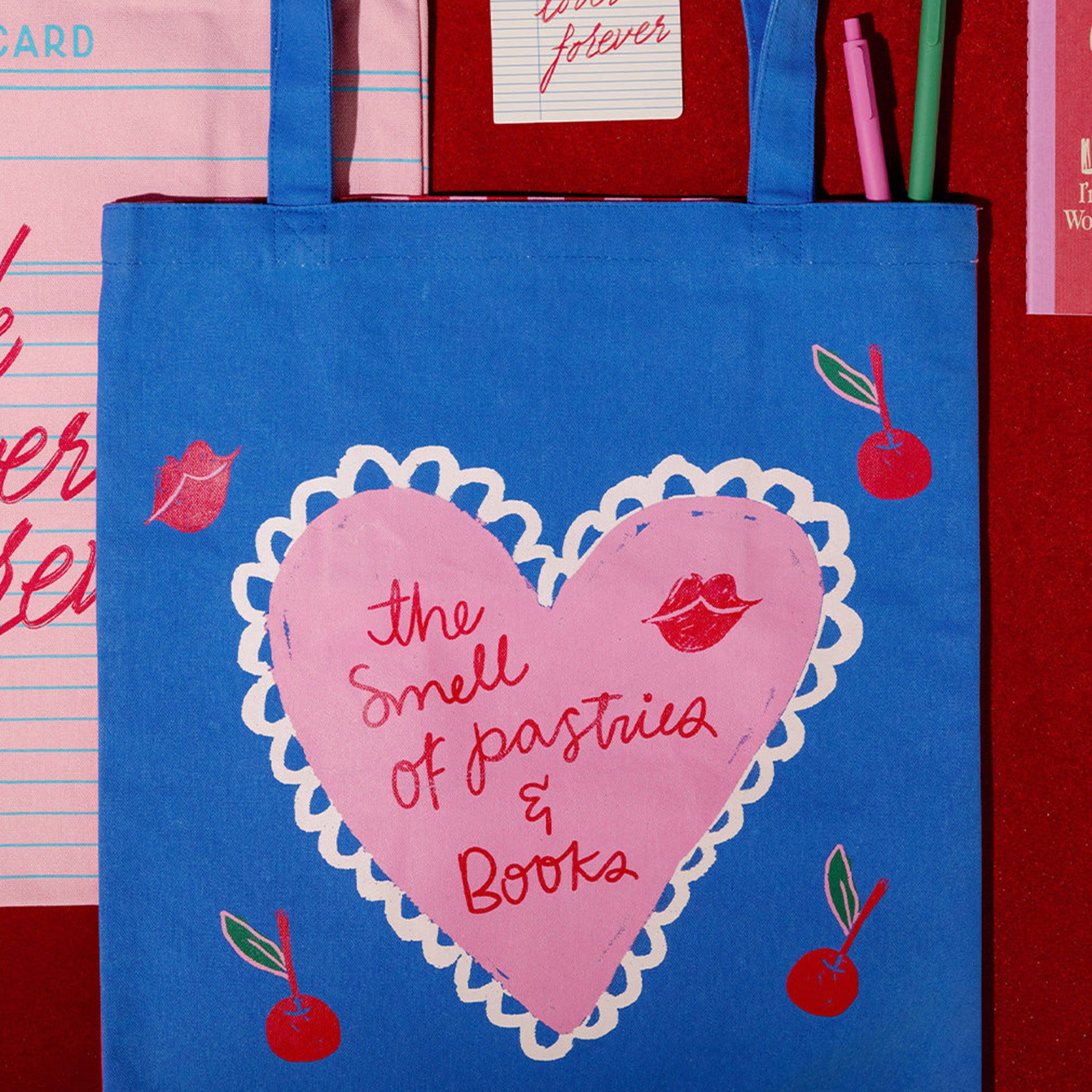 Blue tote bag with pink heart design and text 'The Smell of Pastries & Books' on a red background.