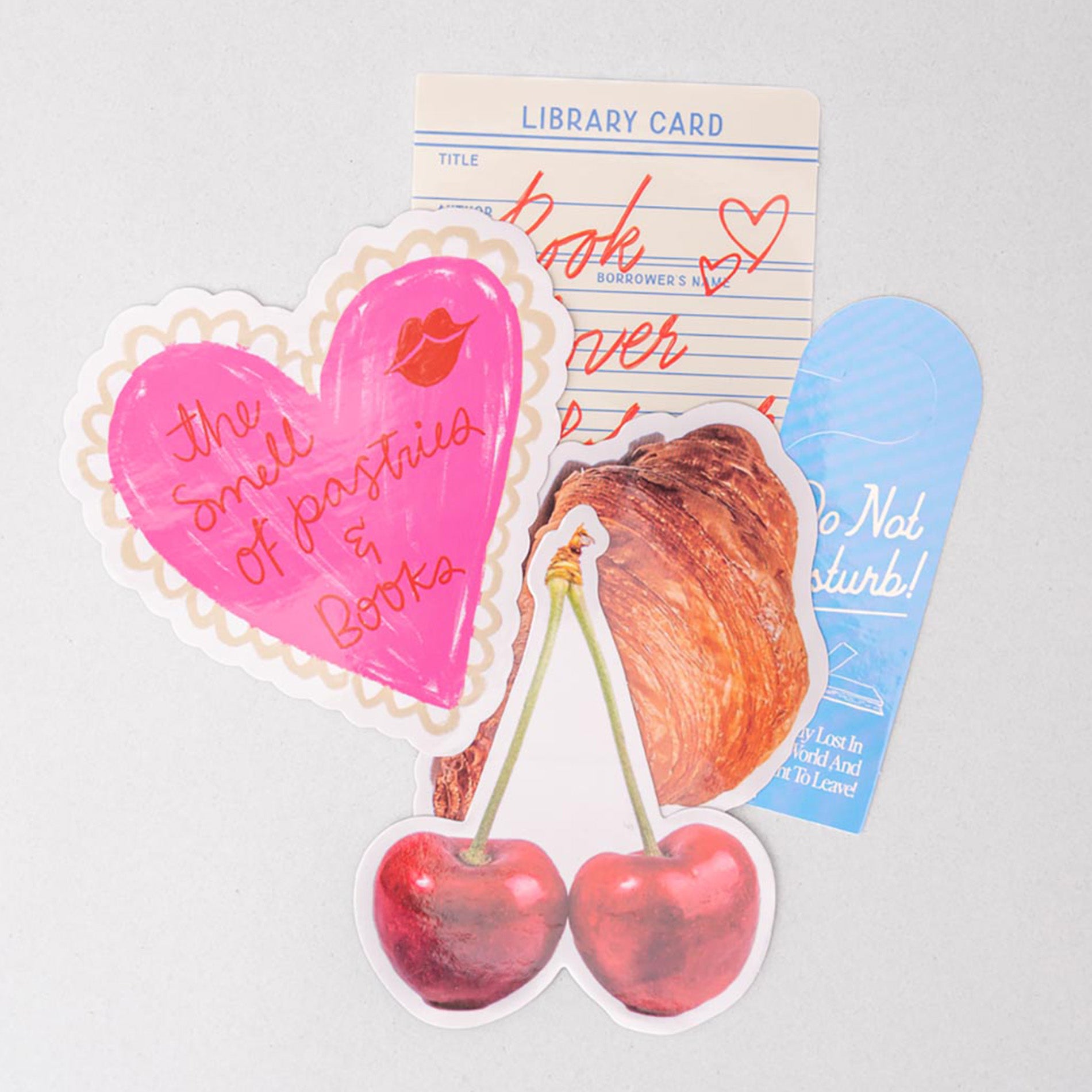 Set of colorful stickers with heart, cherry, library card, pastry, and bookmark on a light gray background.
