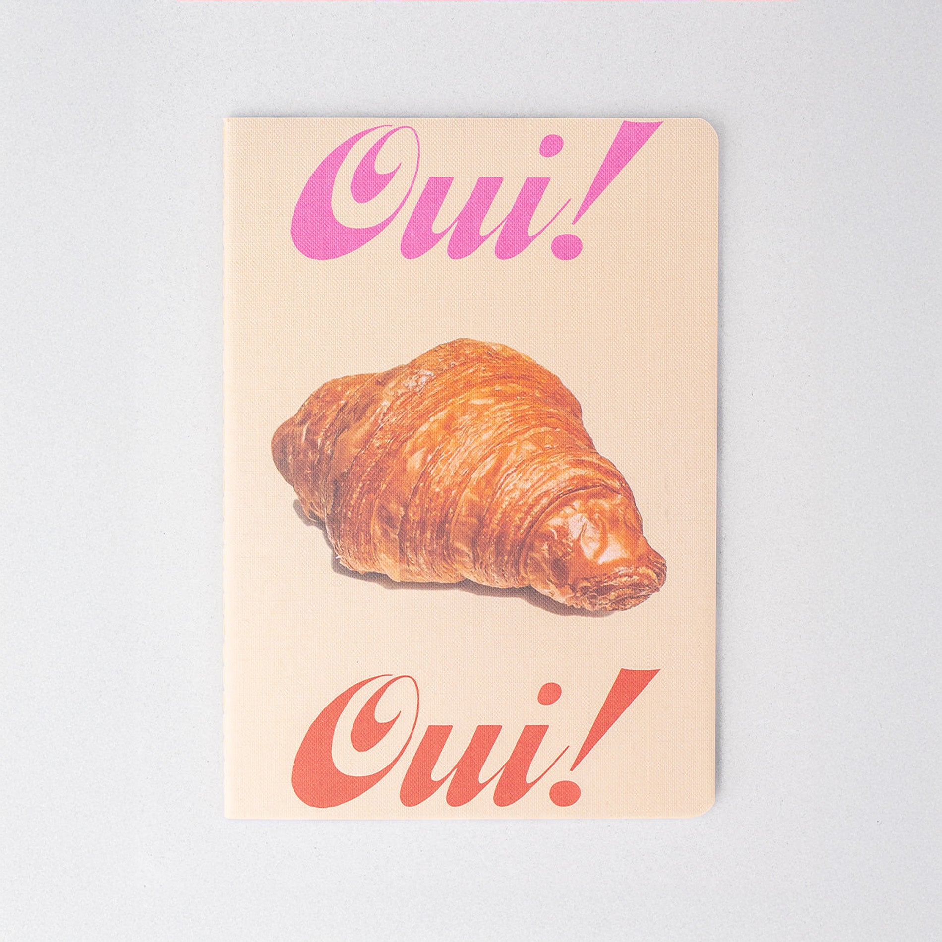Notebook with a croissant and 'Oui!' text on a light background