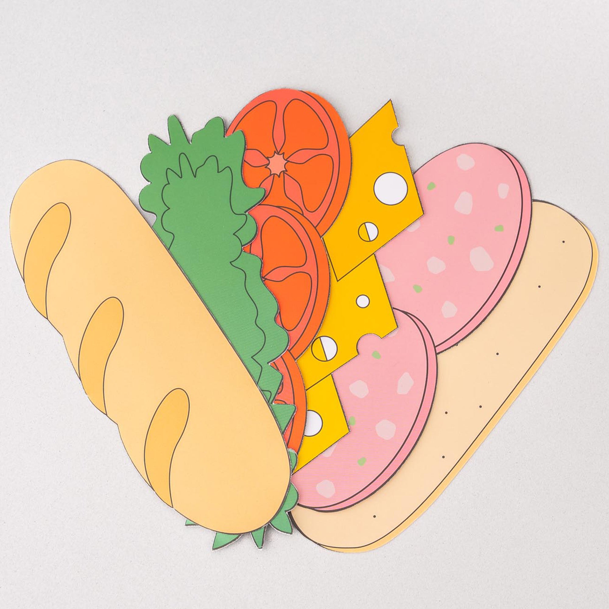 Colorful paper cutout of a sandwich with bread, lettuce, tomato, cheese, and meat on a light gray background