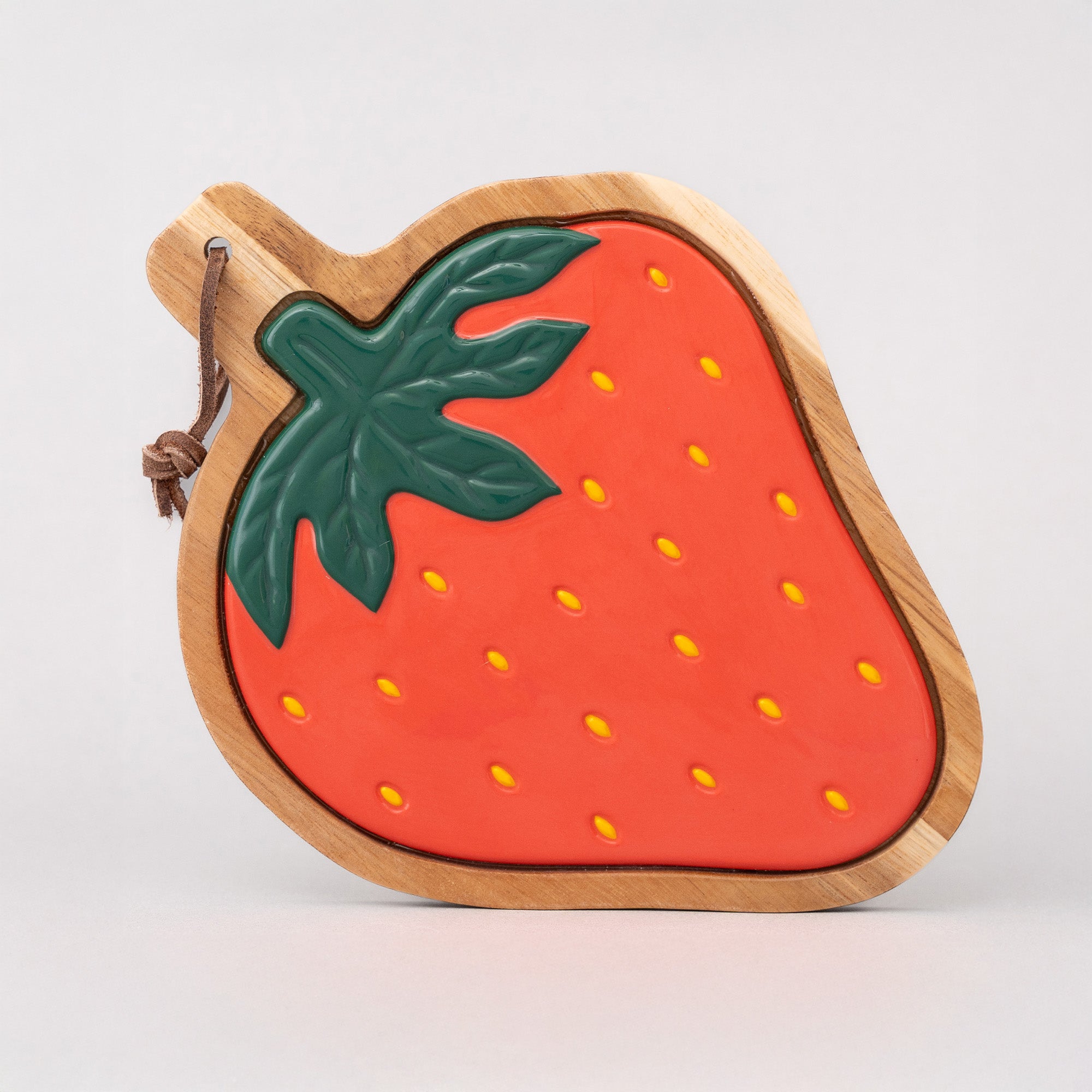 Strawberry-shaped wooden trivet with a green leaf on a light gray background