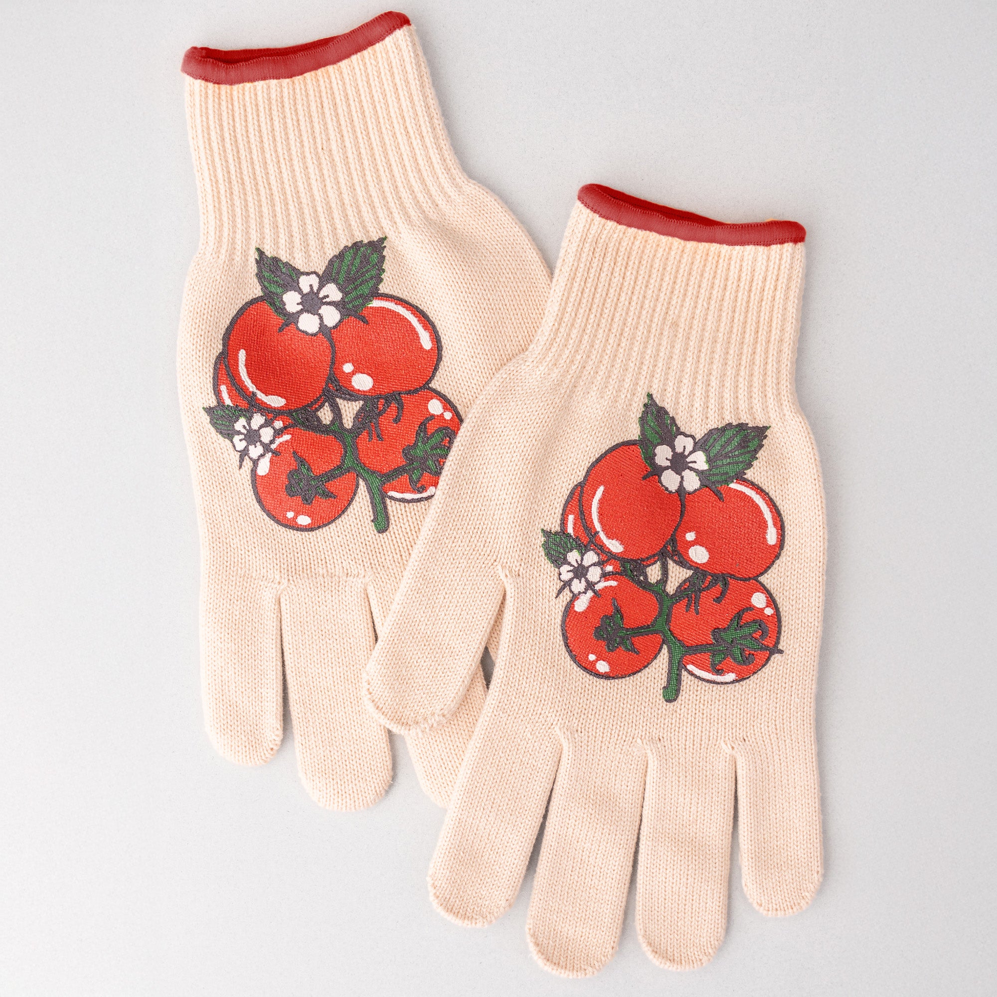 Pair of beige gardening gloves with red tomato design on a light gray background