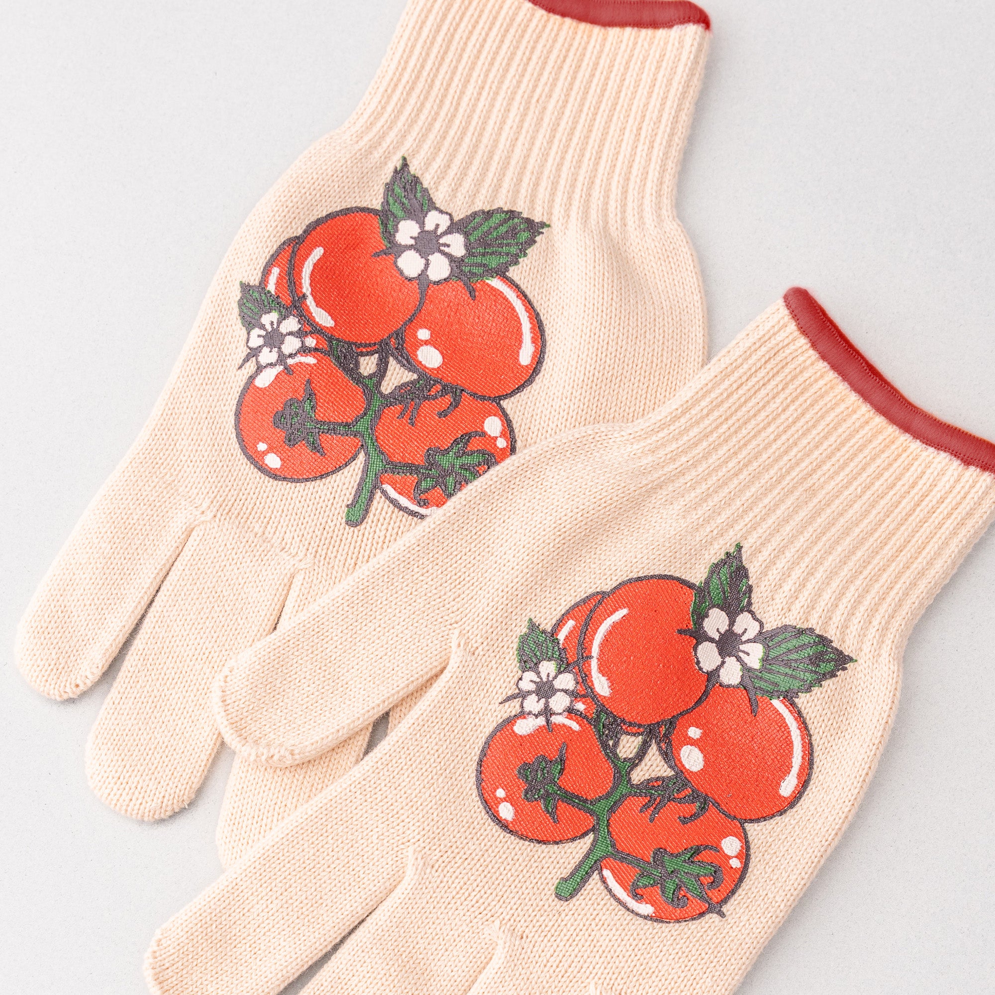 Pair of beige gardening gloves with red tomato design on a light gray background