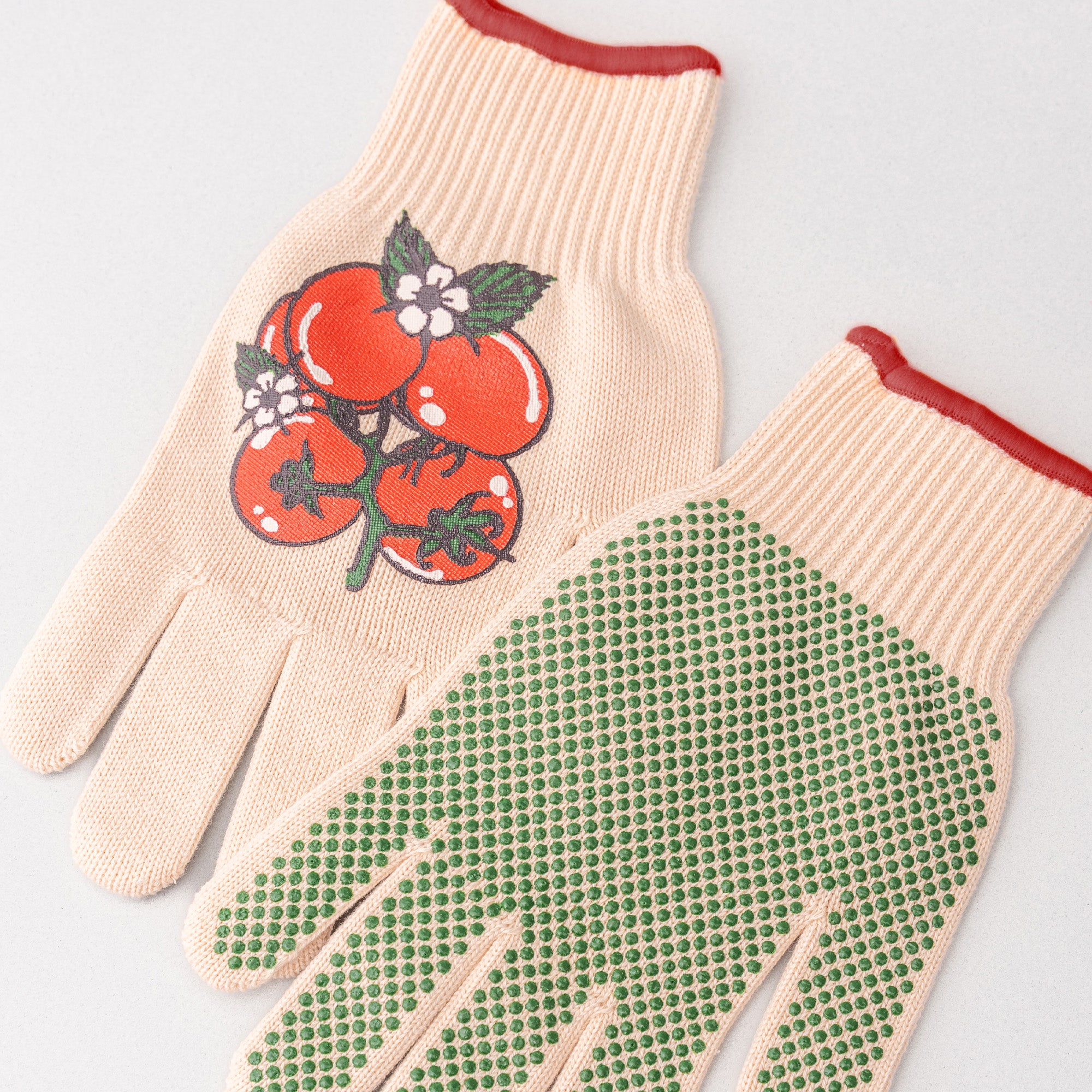 Beige gardening gloves with tomato design on one glove, on a light gray background