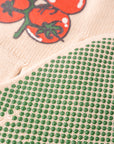 Close-up of green bead pattern on fabric with tomato illustration in the background