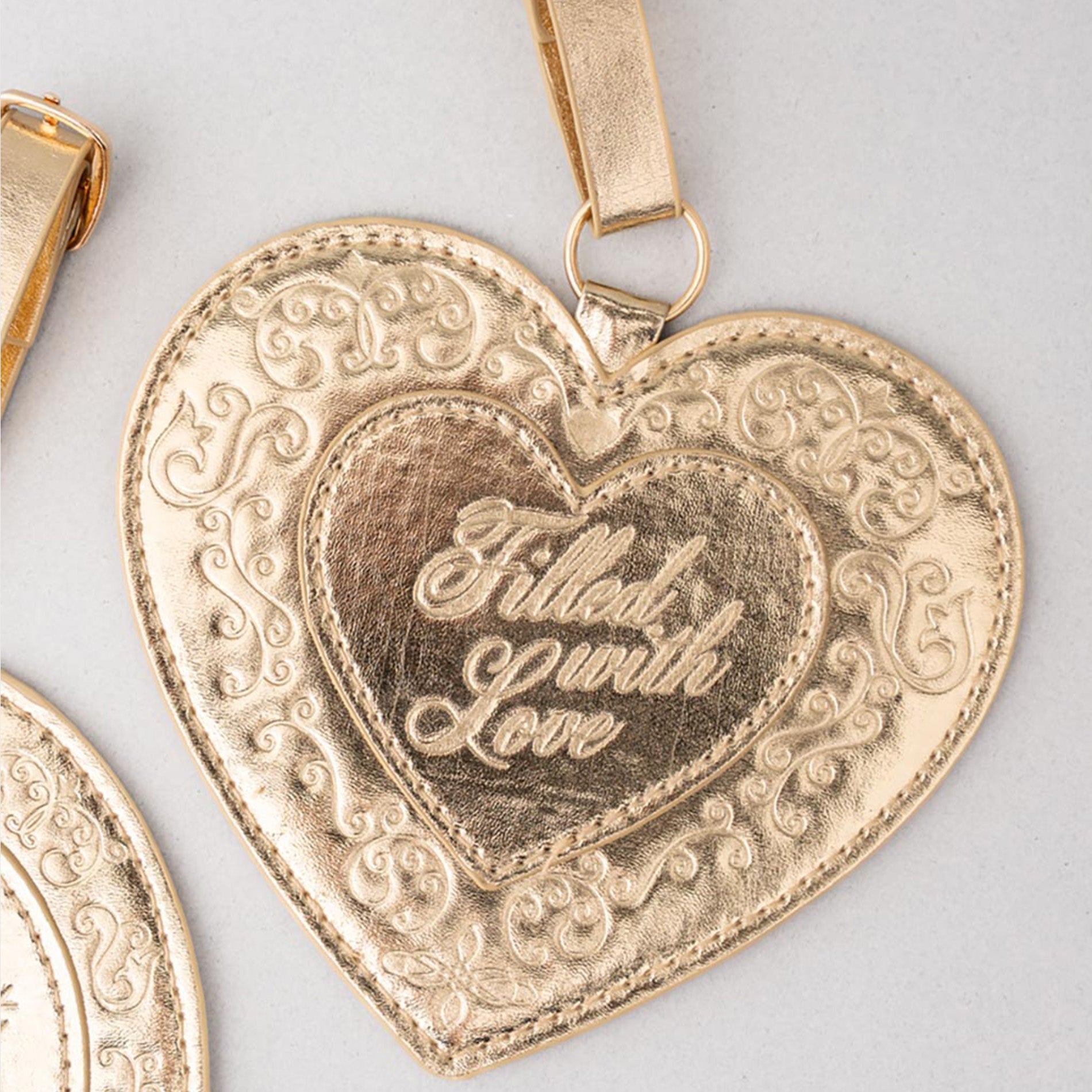 Gold heart-shaped pendant with 'Filled with Love' engraving on a light gray background